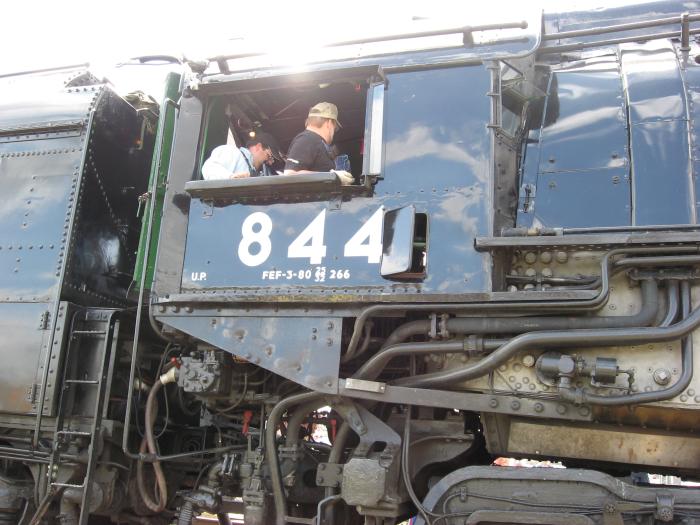 Closeup of cab of 844, showing two crew members and some pipes below the cab
