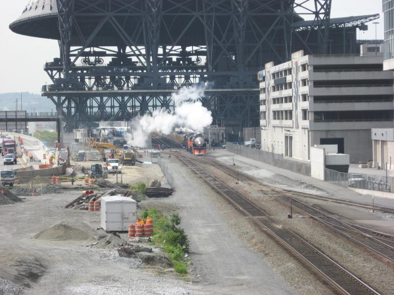 Train hauled by steam locomotives approaching from distance and under Mariners baseball stadium