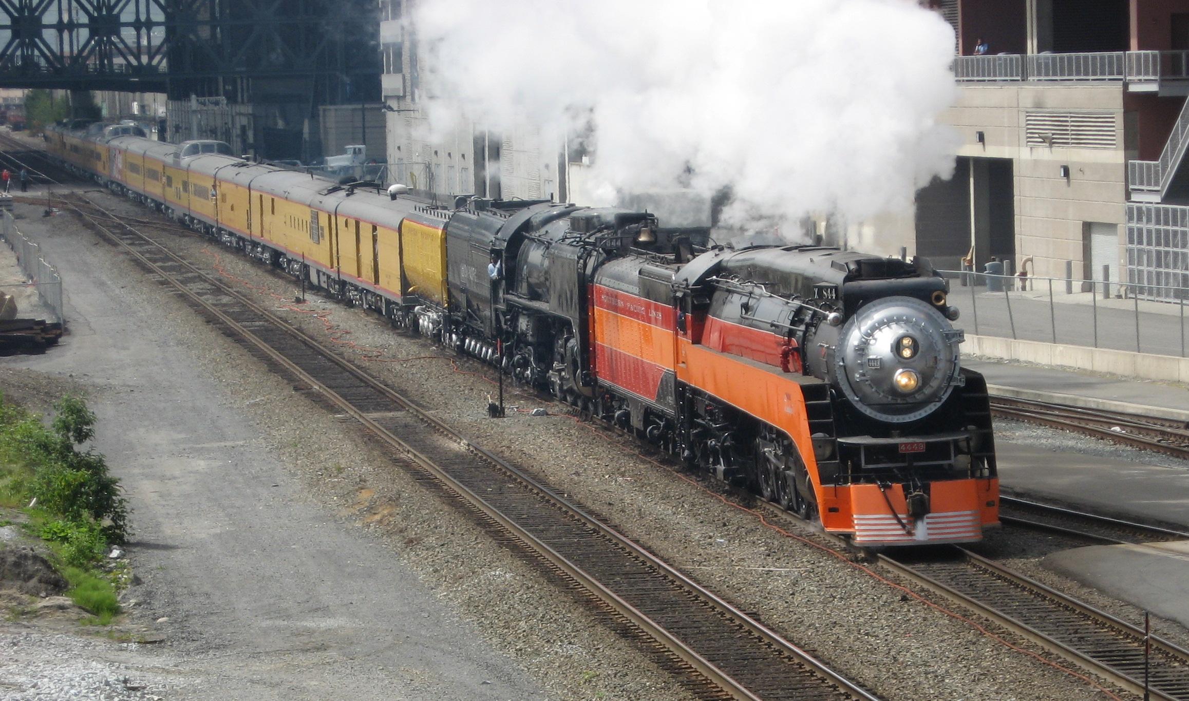 Approaching train led by two steam locomotives and containing yellow passenger cars
