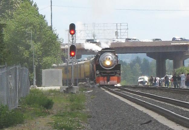 Front end of steam locomotive approaching in the distance, with red signals to the left and bridge above
